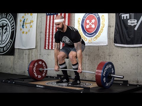 Athlete performing a deadlift with a StrongArm conventional deadlift bar and bumper plates in a gym setting.